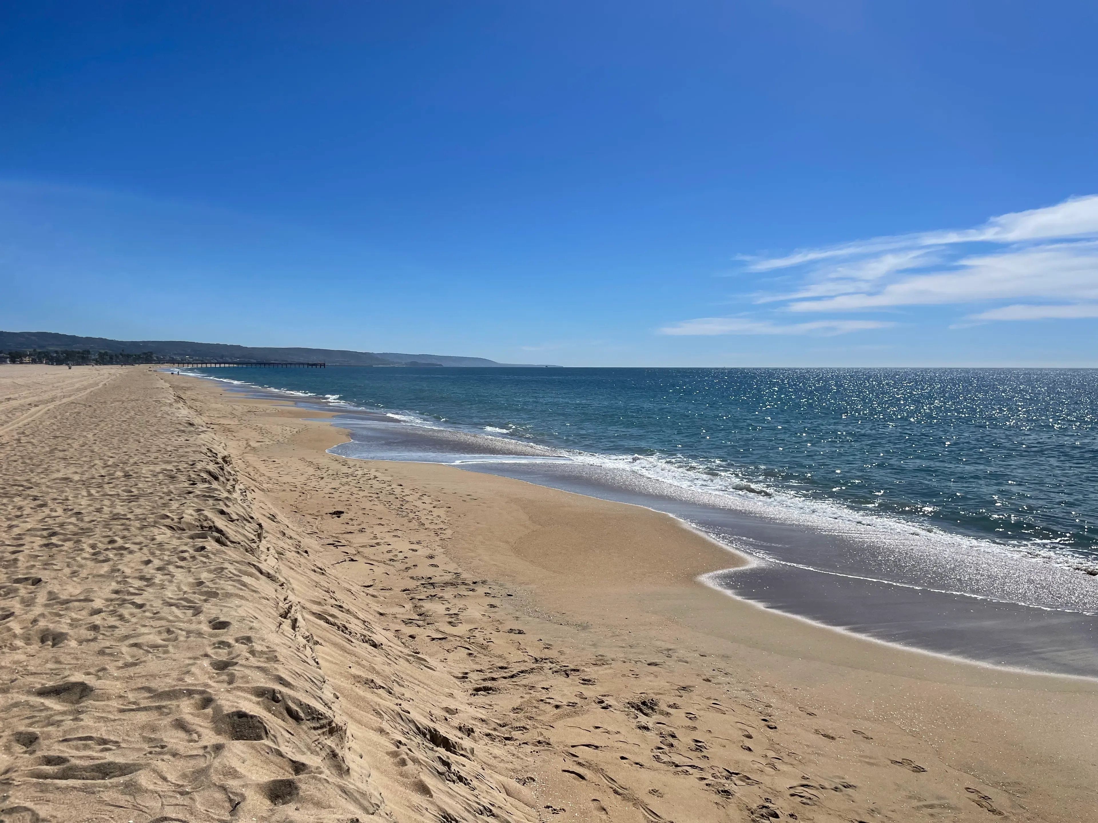 A wide, empty Southern California beach with footprints in the sand and calm ocean waves