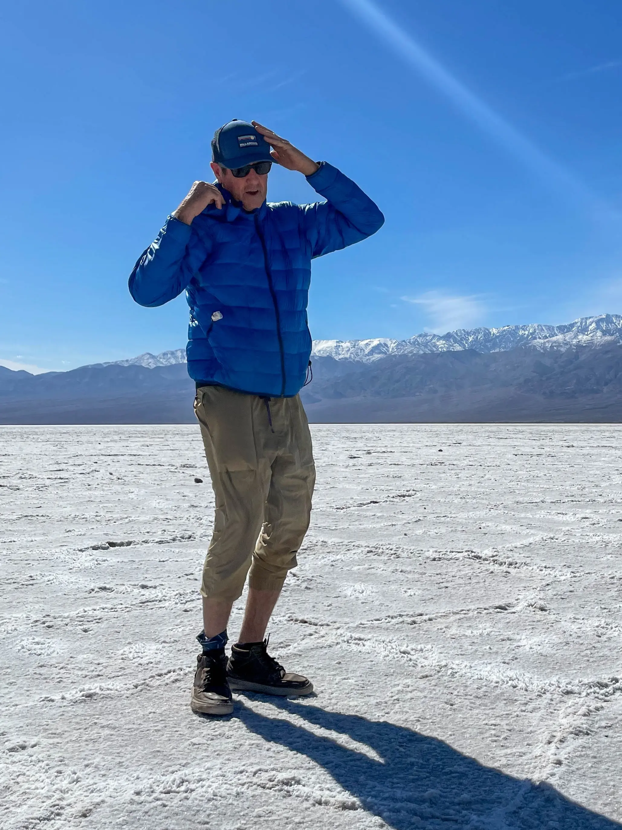 Founder Scott Swift standing on a desert salt flat, shielding his eyes, with snow-capped mountains on the horizon behind him
