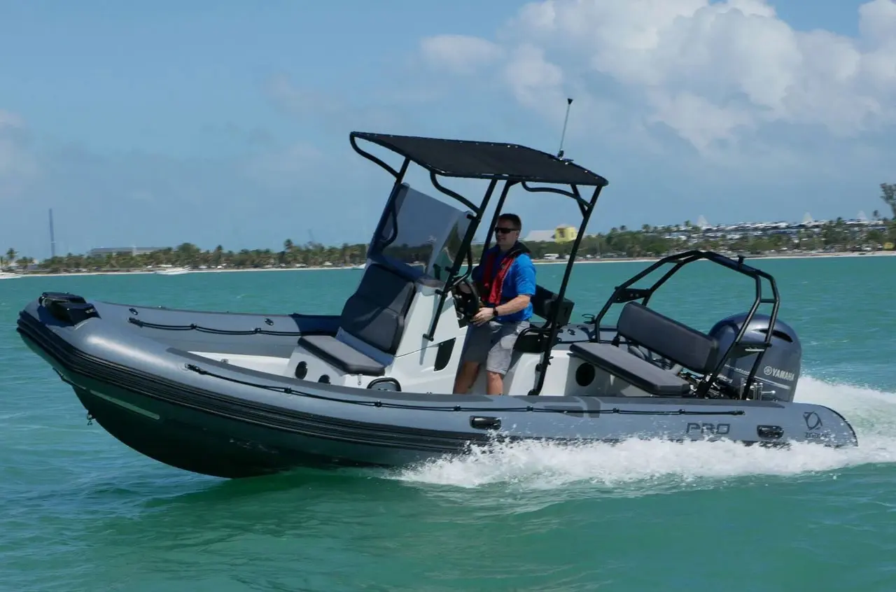 A gray Zodiac inflatable boat with a Yamaha outboard motor speeding across turquoise water, its driver in a life jacket under a black canopy