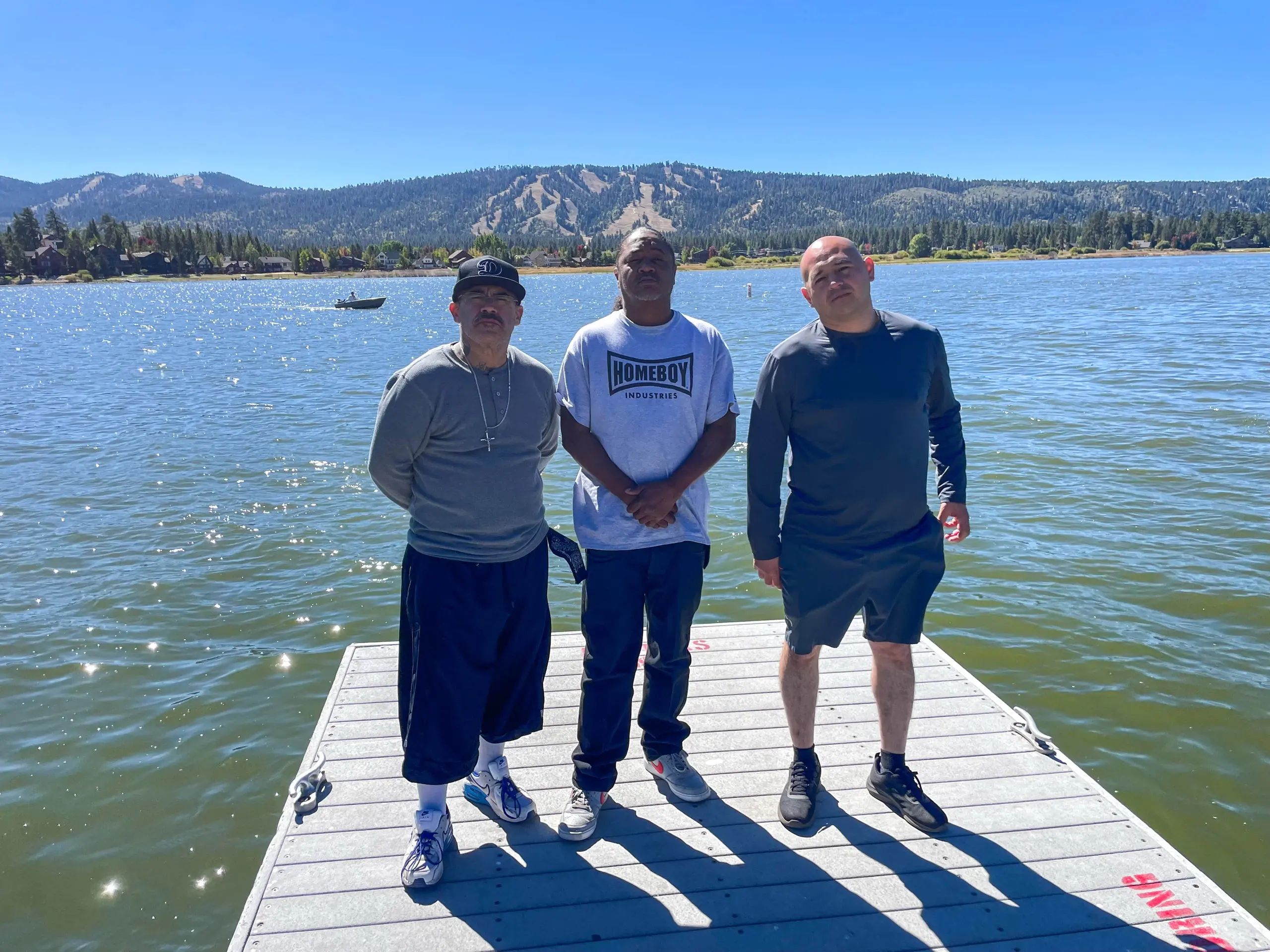 Three participants stand on a floating dock on Big Bear Lake, with a boat on the water and ski-run hills across the lake