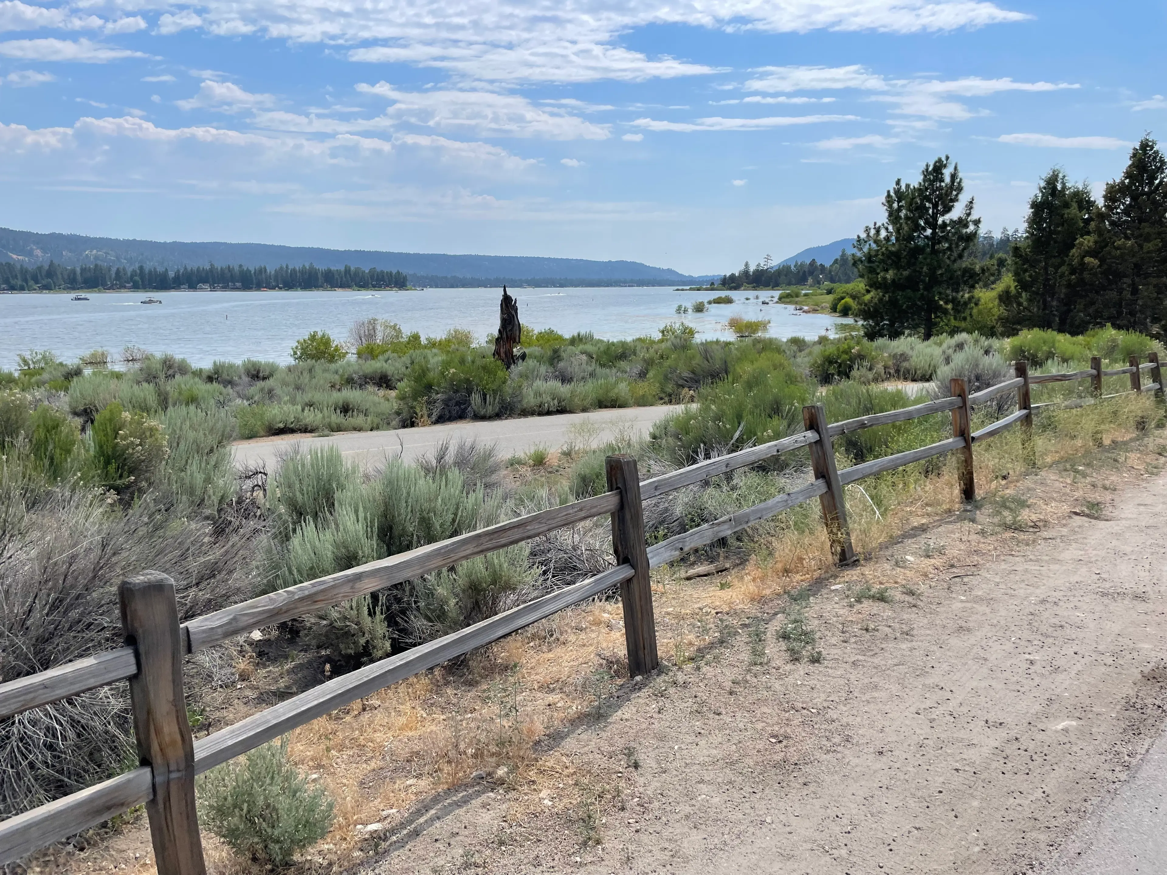 Big Bear Lake from a lakeside trail, with a split-rail fence and sagebrush in front and pine-covered hills along the far shore
