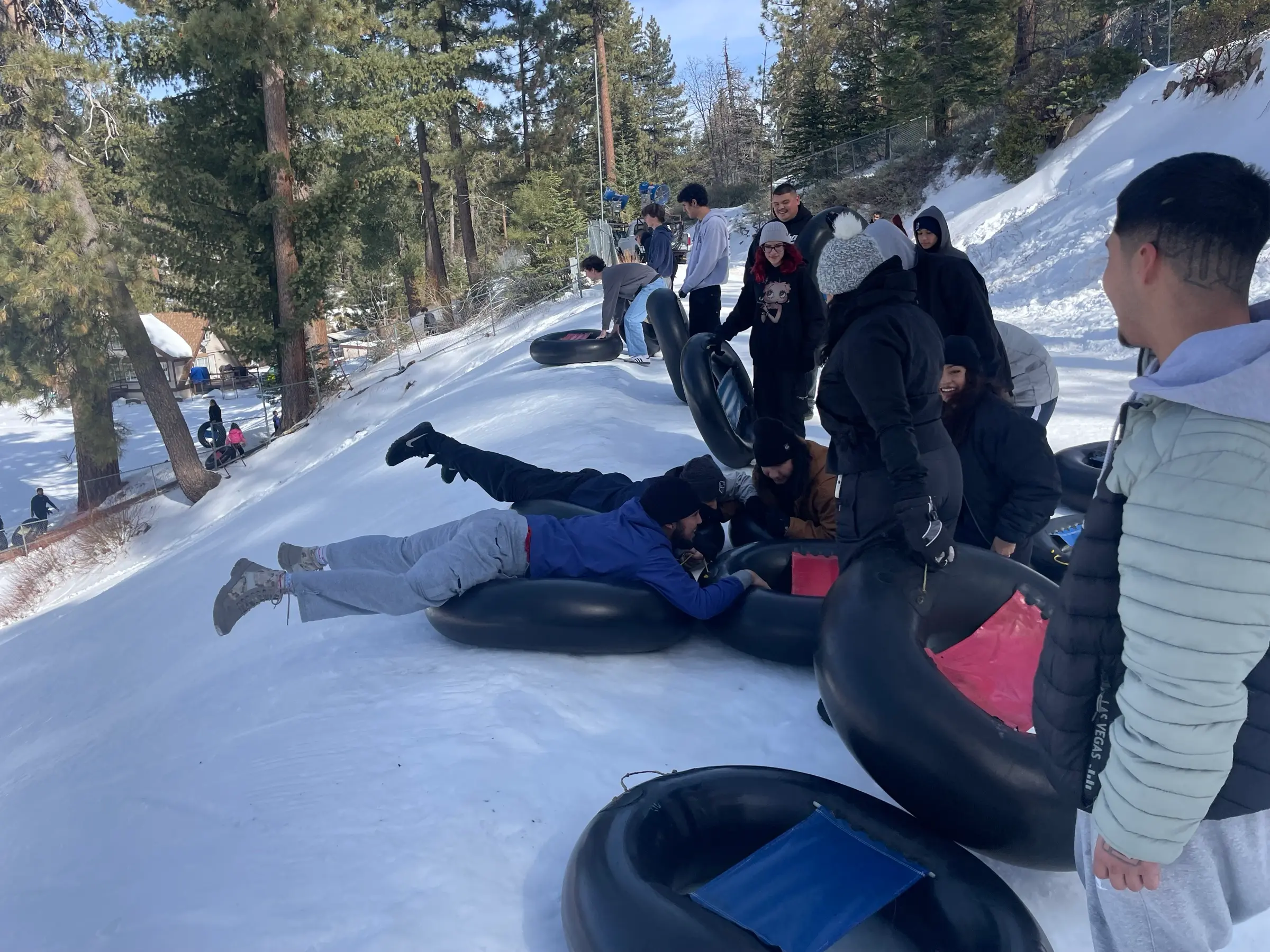 A group of participants lines up with black snow tubes on a snowy slope in Running Springs, two of them sliding off headfirst