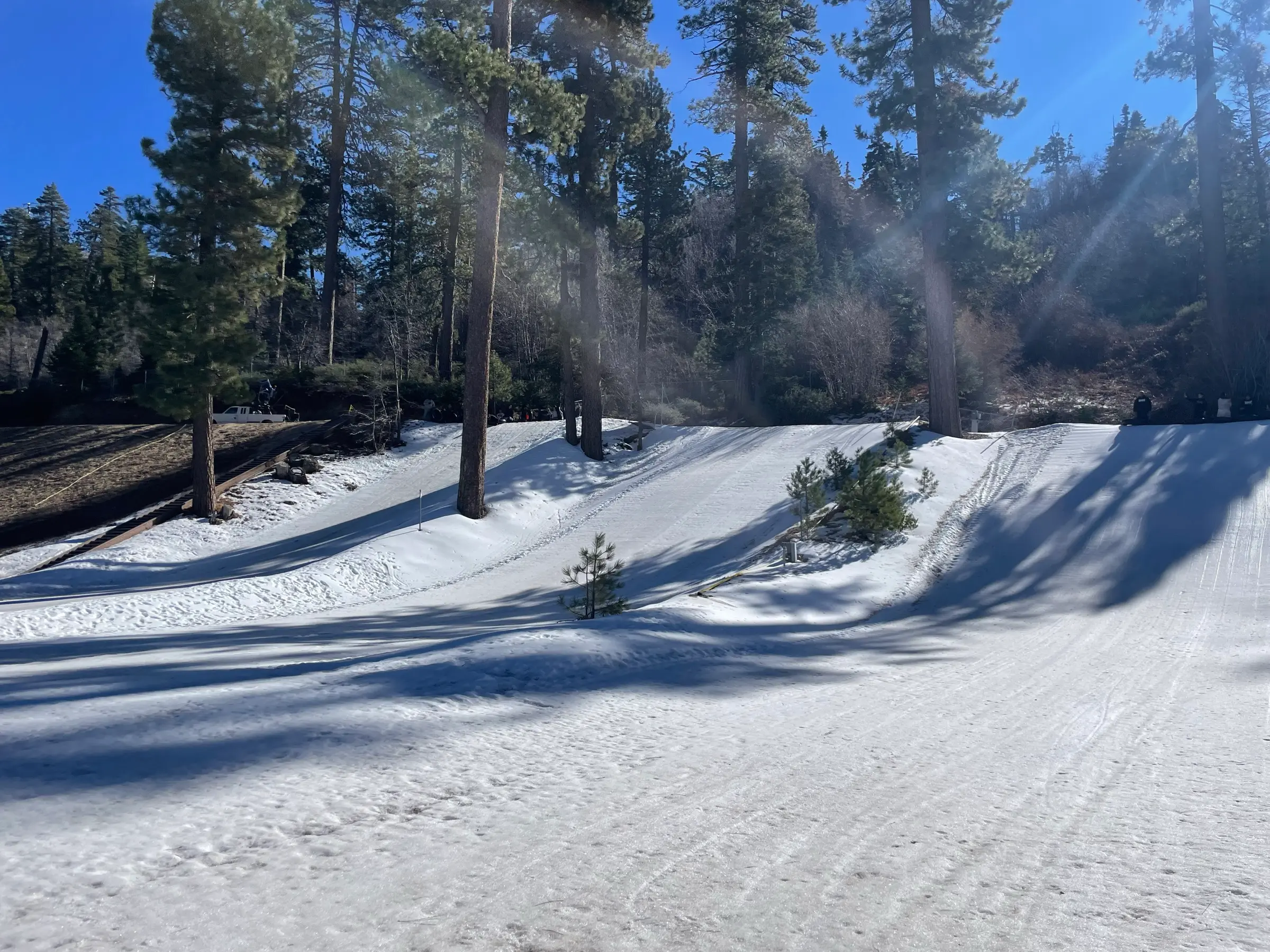 Groomed snow-tubing lanes on a sunlit hillside in Running Springs, with tall pines behind