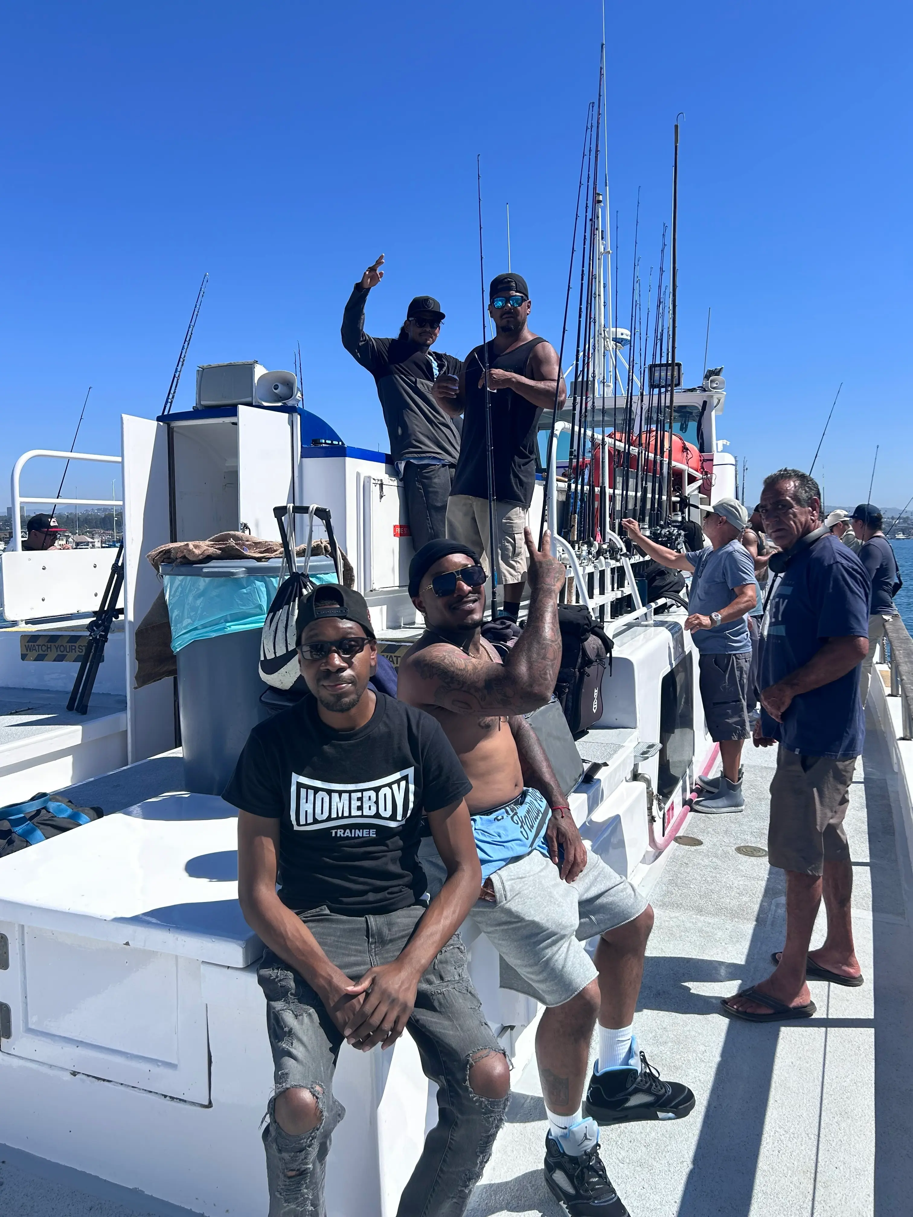Participants gather on the deck of a sportfishing boat in Newport Harbor, rods racked behind them under a clear blue sky