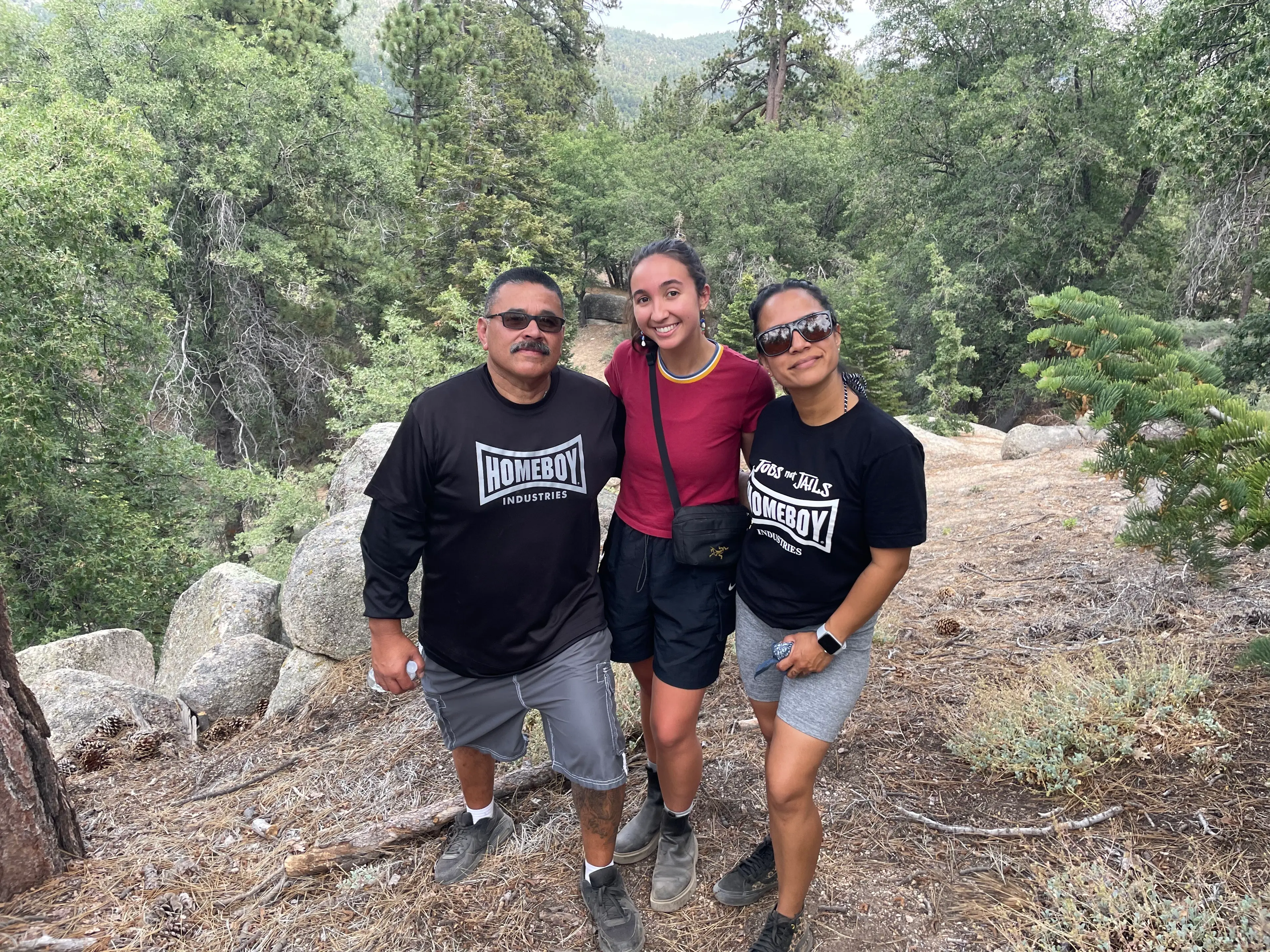 Three hikers smiling together on a trail among boulders and pine trees