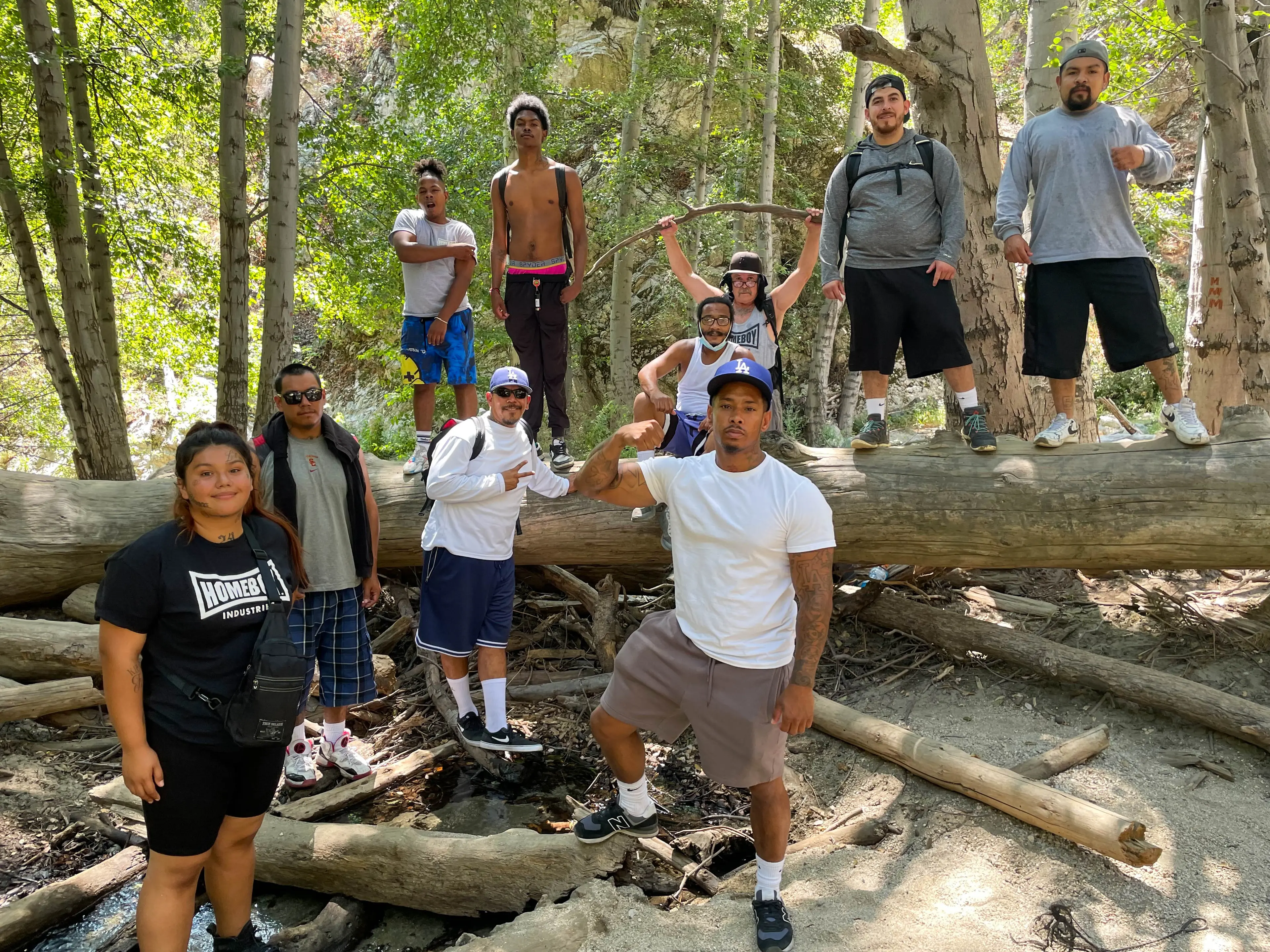 A group of hikers gathered around a fallen log in the Angeles National Forest, some standing on it and others posing in front