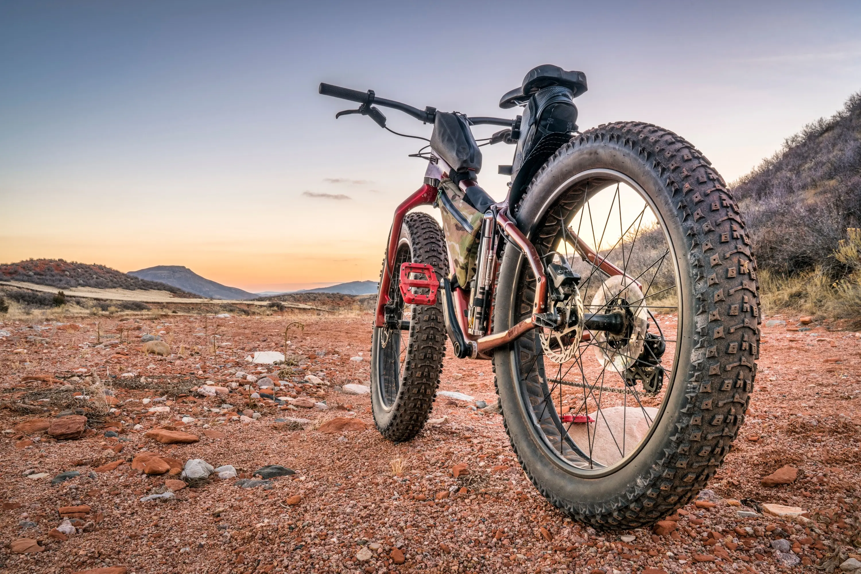 A fat-tire bike parked on red, rocky desert ground at sunset