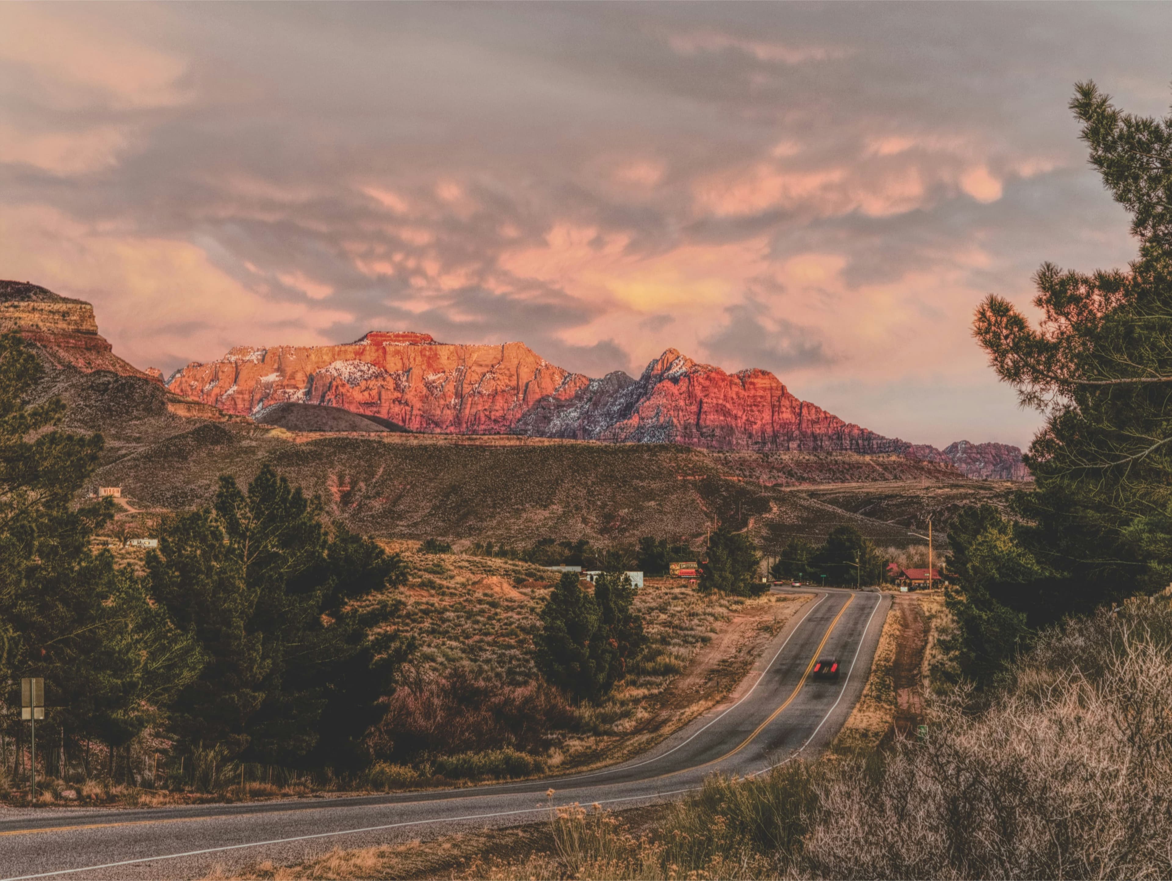 Desert highway leading toward red rock cliffs under a vivid sunset sky